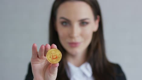 Pretty-young-woman-in-black-jacket-demonstrating-bitcoin-and-looking-at-camera