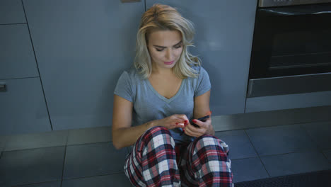 Charming-woman-with-smartphone-on-kitchen-floor