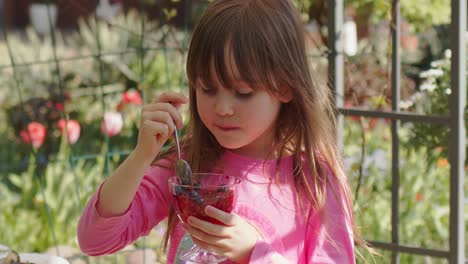 Cute-little-6-or-7-years-old-girl-eating-fruit-dessert-jelly-in-summer-garden--Slow-motion-video