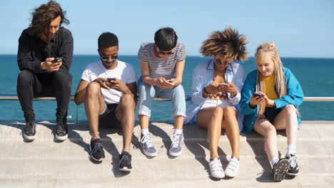 Contemporary-diverse-friends-with-smartphones-on-seafront