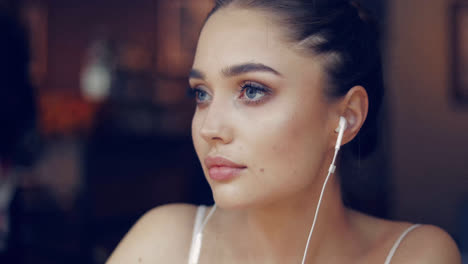 Young-gentle-girl-posing-in-headphones-and-looking-away-while-sitting