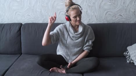 Adorable-middle-aged-blond-woman-sitting-on-sofa-in-her-home-and-listen-to-the-music