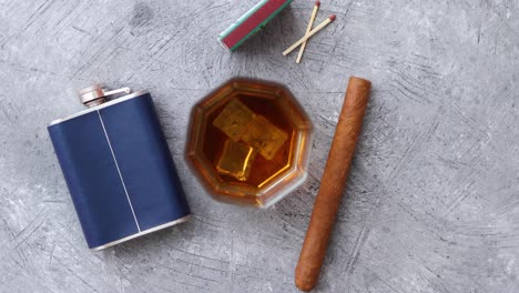 Glass-of-whiskey-with-ice--big-cuban-cigar--matches-and-hip-flask